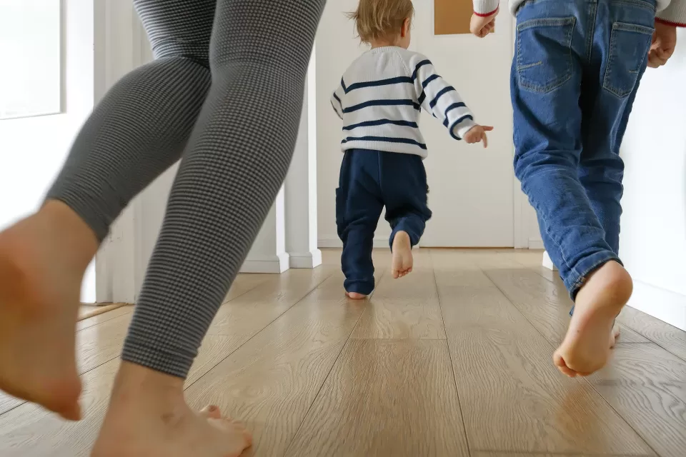 Close-up of two adults running after a small toddler in a bright apartment hallway